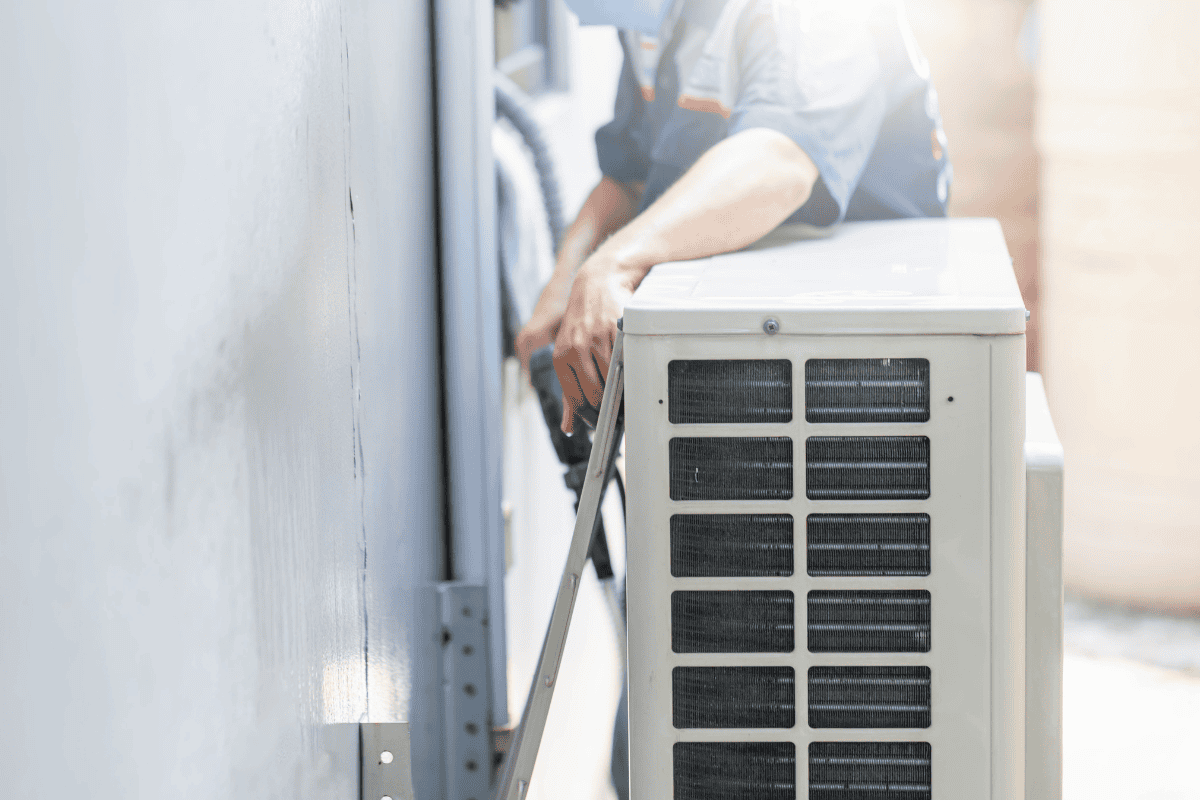 A technician works on an outdoor air conditioning unit, adjusting wiring and components. The sunlight casts a warm glow on the scene, highlighting the technician's hands and the unit's grille.