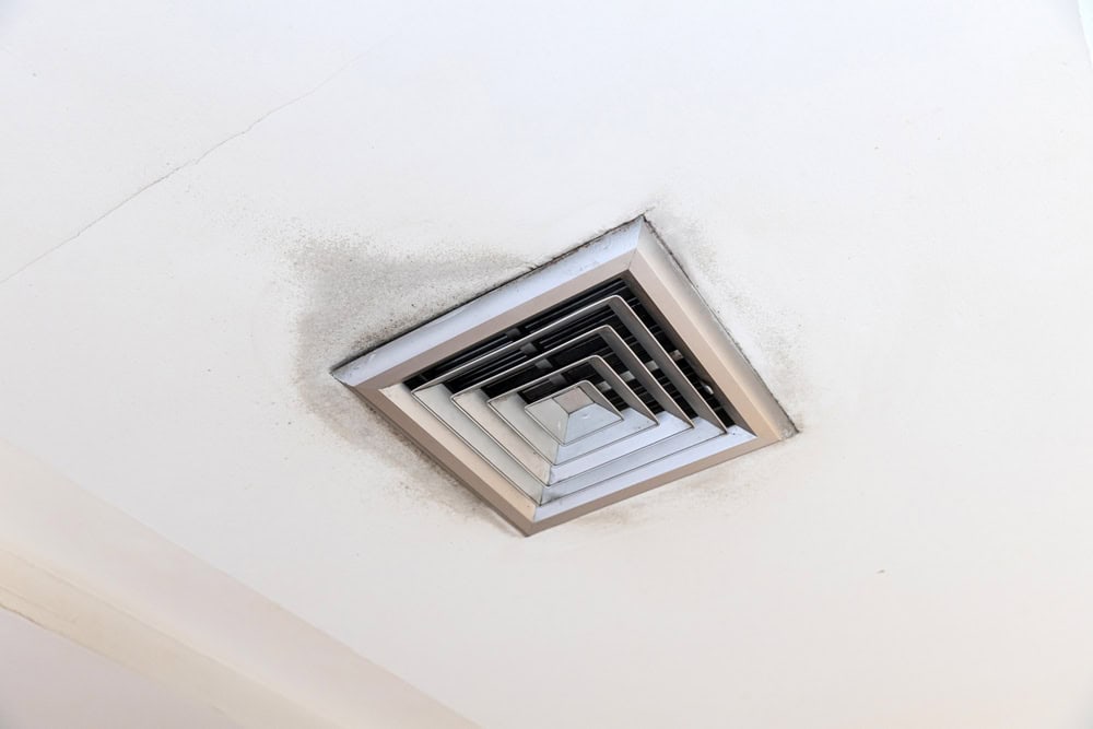 A square ceiling air vent surrounded by dust and dirt accumulation is visible. The vent features several concentric layers, and the ceiling shows signs of wear.